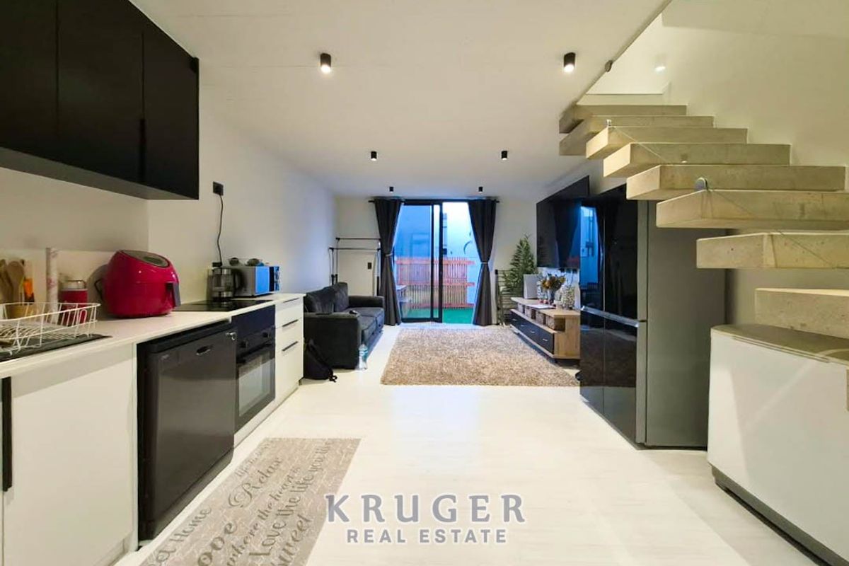 Modern open-plan living area featuring a sleek kitchen, floating staircase with glass balustrade, and sliding doors leading to an outdoor space.