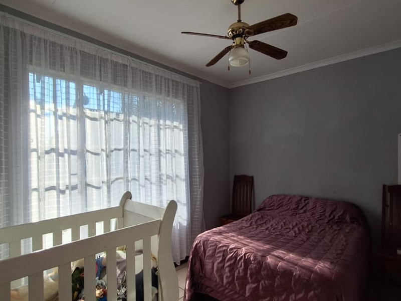 A bedroom featuring tiled flooring and a ceiling fan, with natural light entering through a large window.