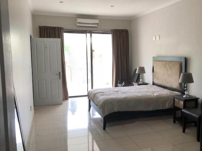 A spacious bedroom featuring tiled flooring, a split-system air conditioner, and a sliding glass door providing access to an outdoor balcony area.