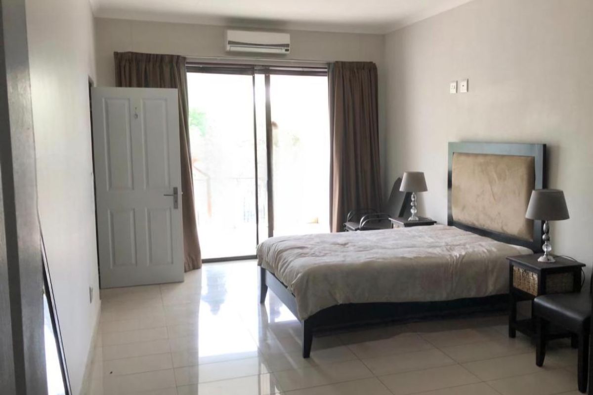 A spacious bedroom featuring tiled flooring, a split-system air conditioner, and a sliding glass door providing access to an outdoor balcony area.