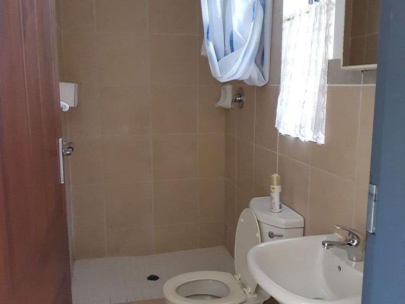 A functional bathroom featuring a pedestal basin, toilet, and a tiled shower area with neutral wall and floor tiles.