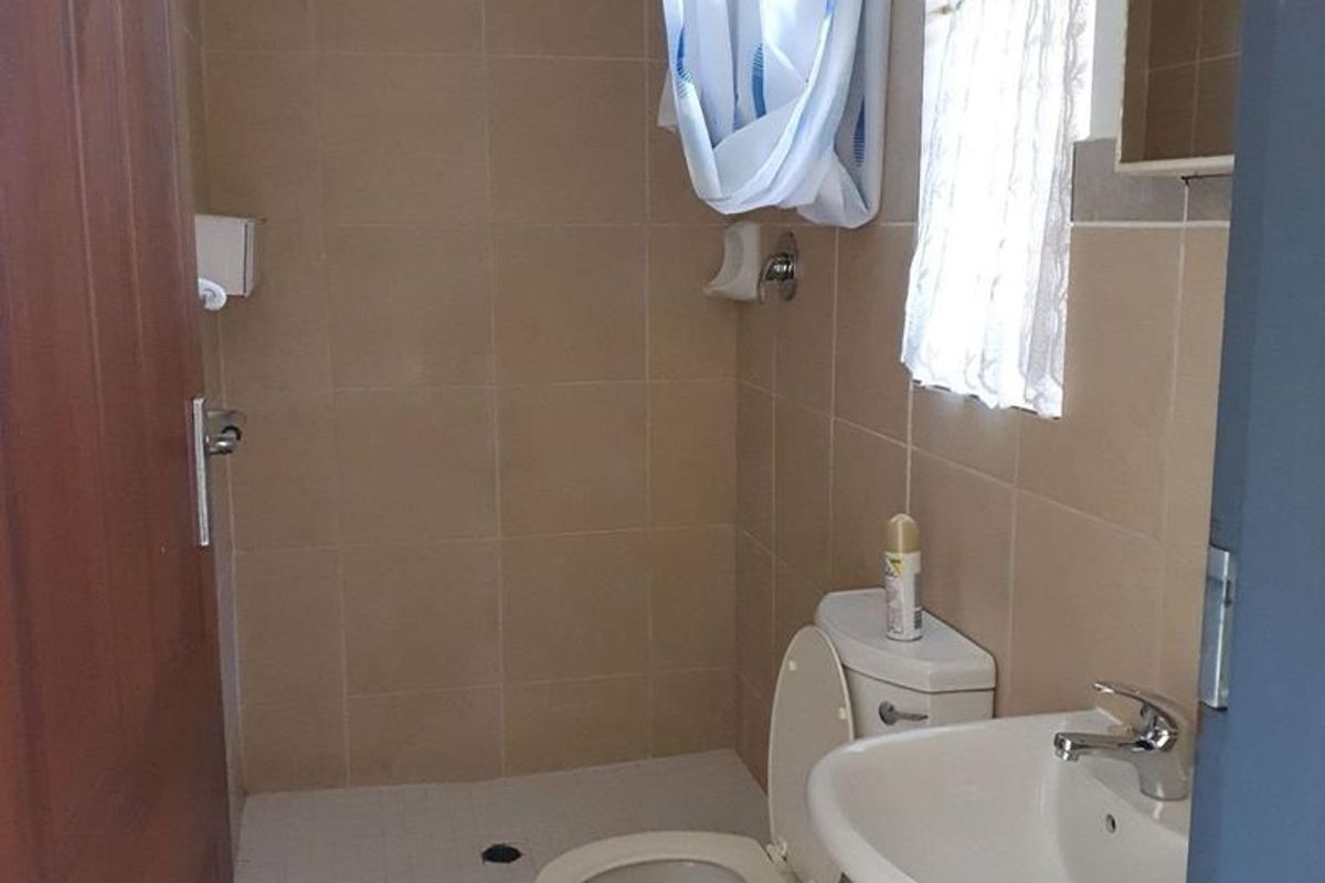 A functional bathroom featuring a pedestal basin, toilet, and a tiled shower area with neutral wall and floor tiles.