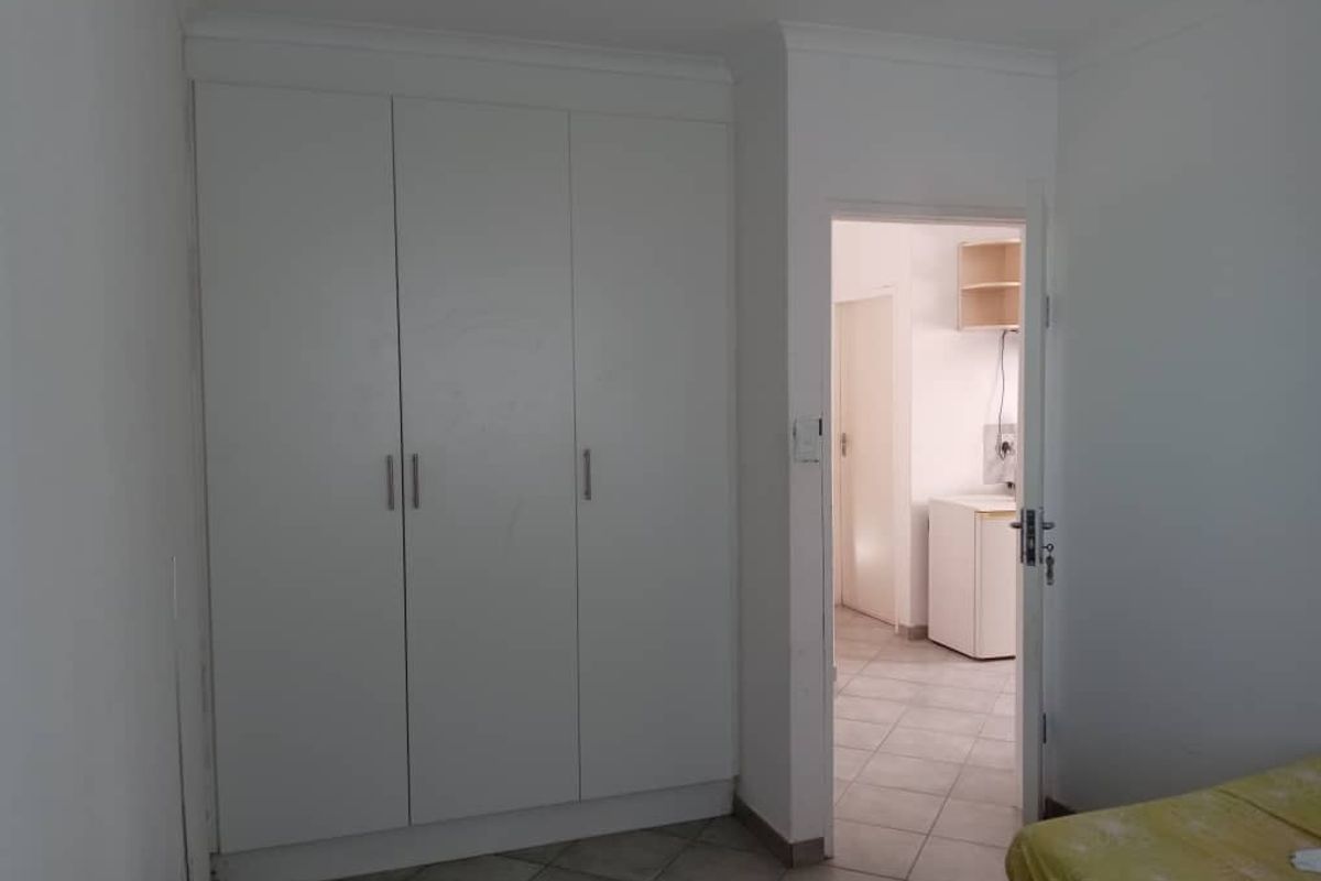 A bedroom featuring built-in white wardrobes and tiled flooring, with a doorway leading to an adjacent utility or kitchen area.