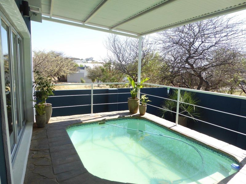 A compact, covered outdoor pool area featuring stone paving, a protective metal railing, and direct access to the main living space.