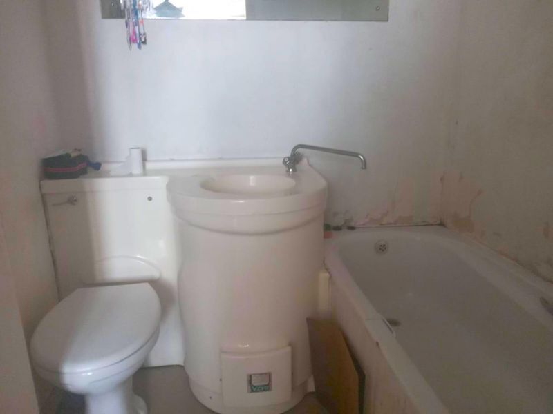 Compact bathroom featuring an integrated toilet and basin unit alongside a standard bathtub, requiring cosmetic updates and wall repairs.