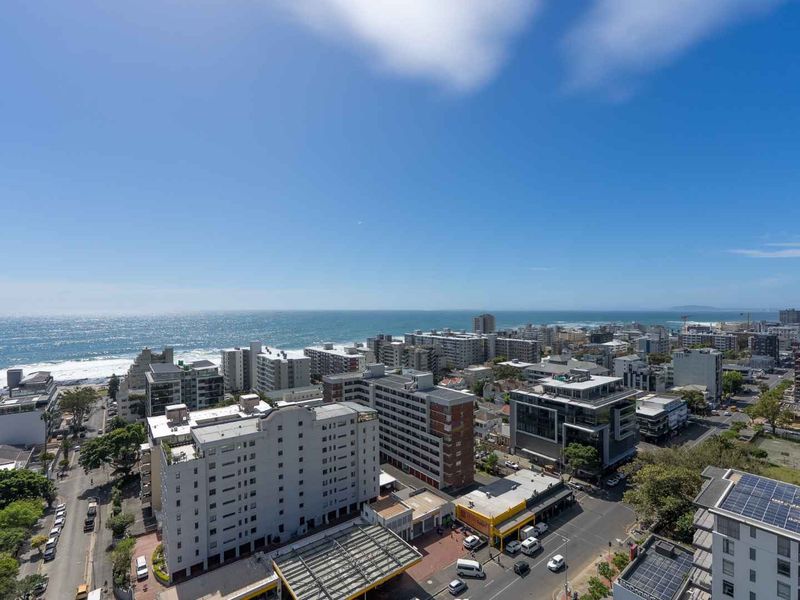 Elevated aerial view overlooking the coastal urban landscape, featuring city buildings and a clear view of the ocean horizon.
