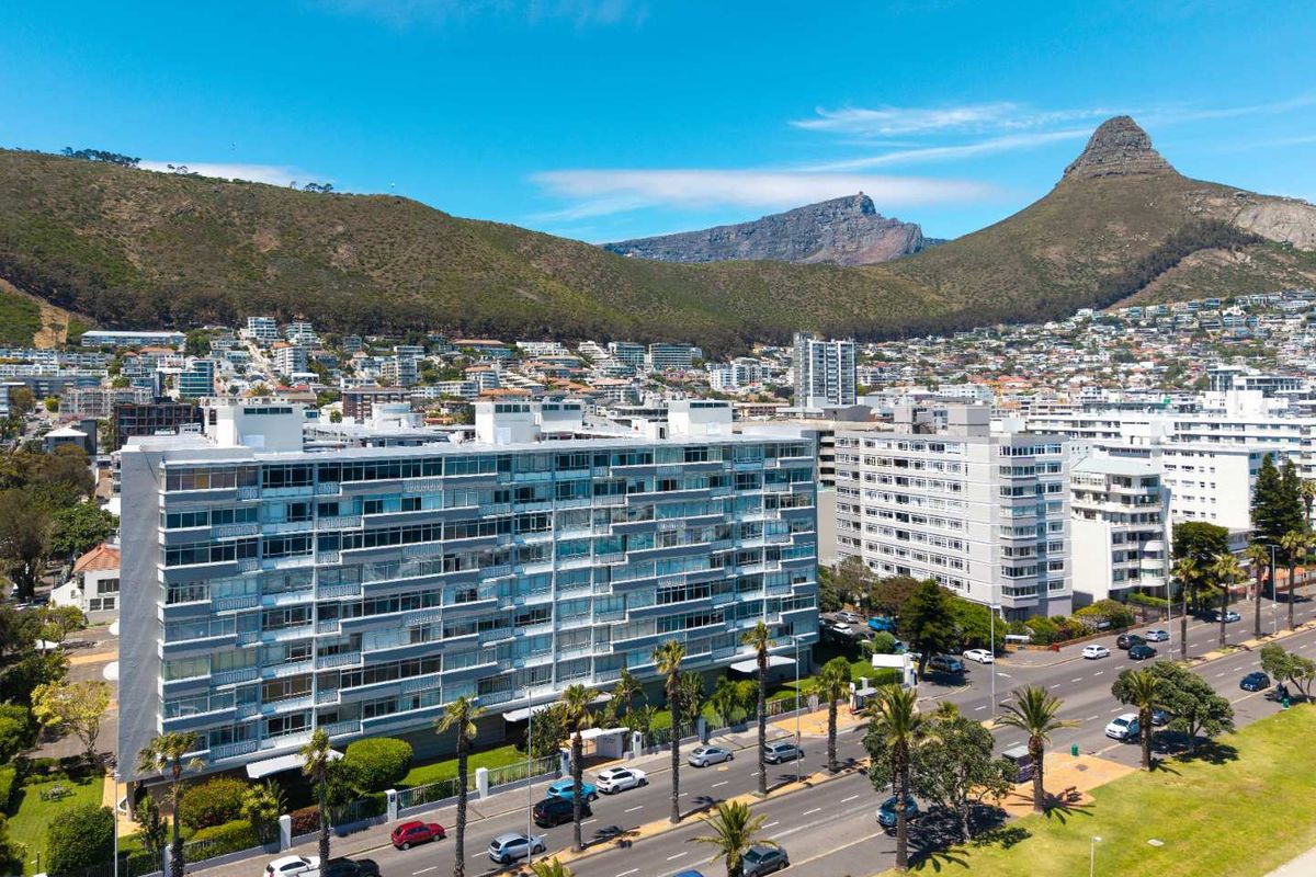 Aerial view of a multi-story apartment complex situated along a coastal road with mountain views in the background.