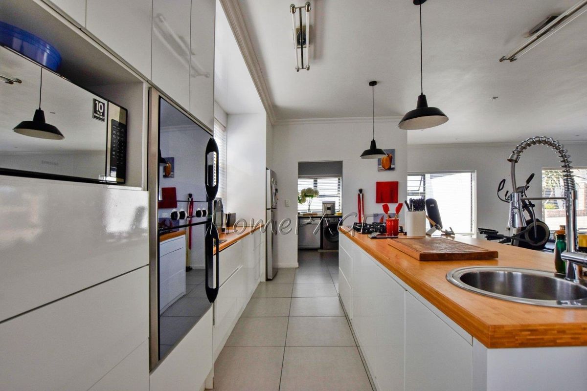 Modern kitchen featuring sleek white cabinetry, wooden countertops, a central island with a sink, and integrated appliances, leading to a separate scullery area.