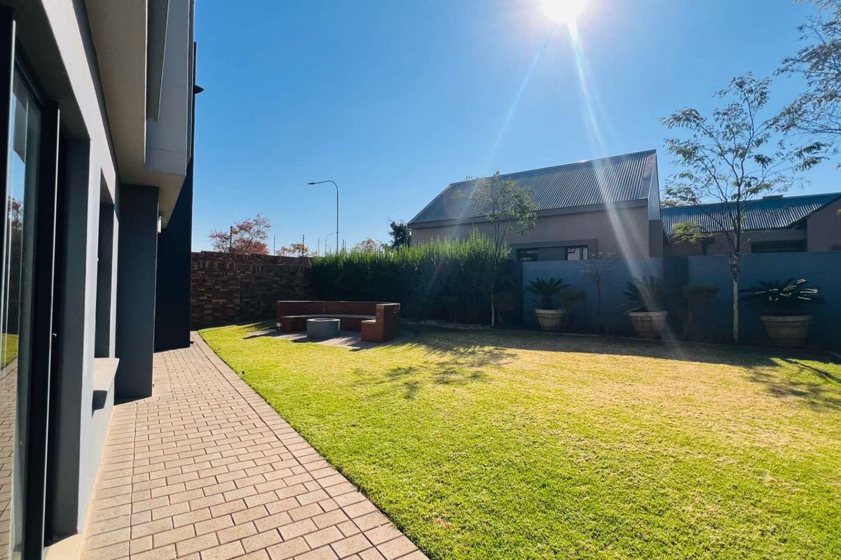 A well-maintained rear garden featuring a paved patio area, a manicured lawn, and a built-in brick seating feature against the boundary wall.
