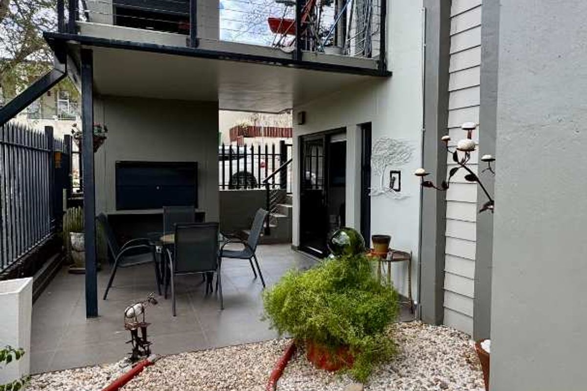 A multi-level outdoor living space featuring a ground-floor patio area and an elevated balcony with a built-in braai, set within a landscaped garden.