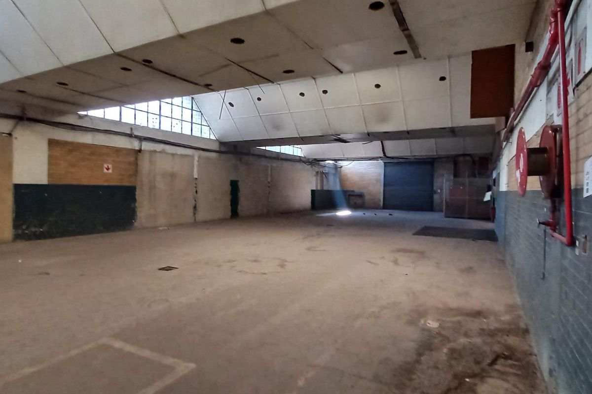 Spacious industrial warehouse area featuring high vaulted ceilings, exposed brick walls, concrete flooring, and integrated fire suppression system.