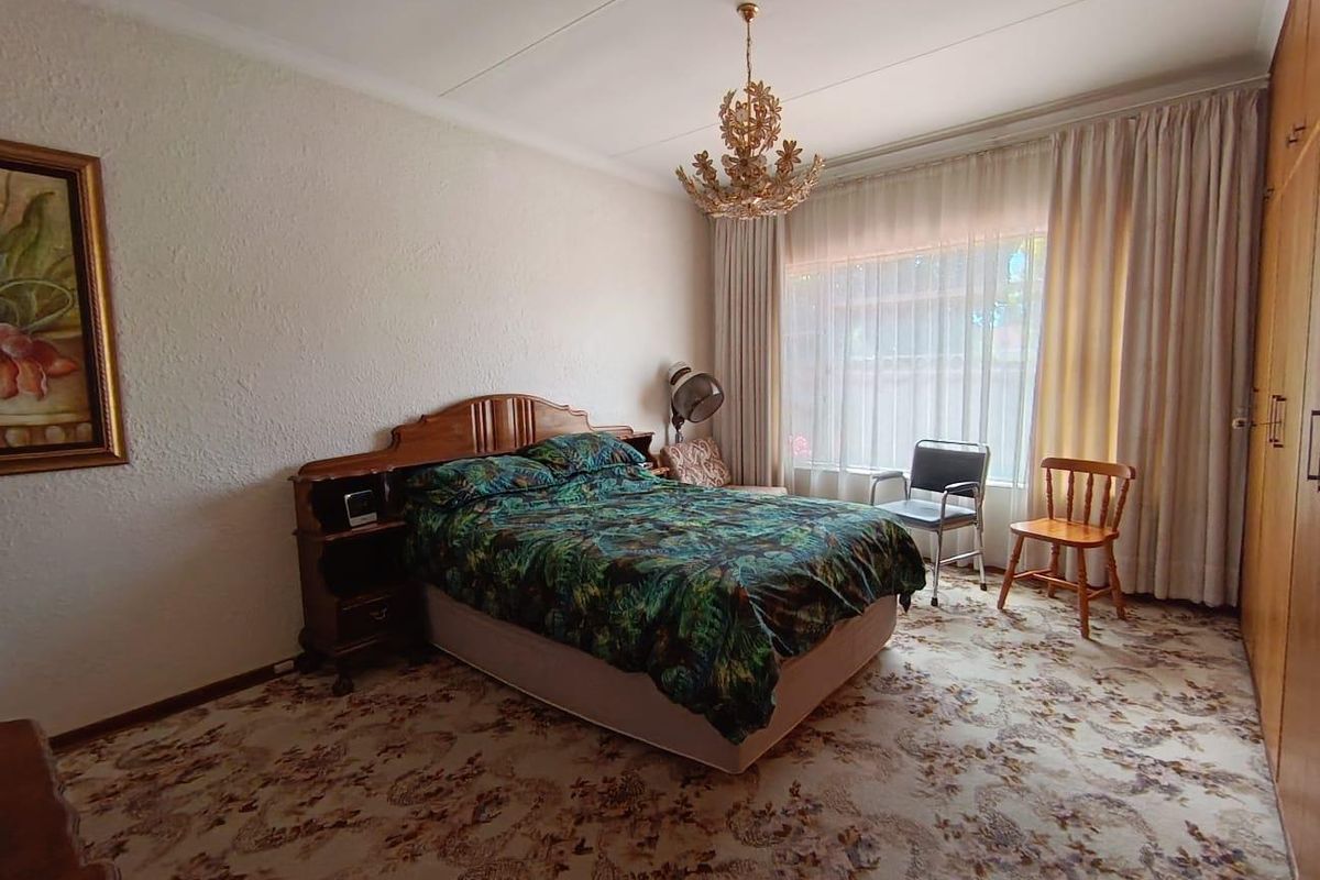 A spacious bedroom featuring built-in cupboards, carpeted flooring, and large windows with curtain tracks, offering a classic layout ready for modernization.