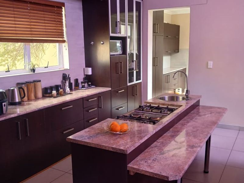 Modern kitchen featuring dark cabinetry, stone countertops, a central island with a gas hob, and an adjoining scullery area.