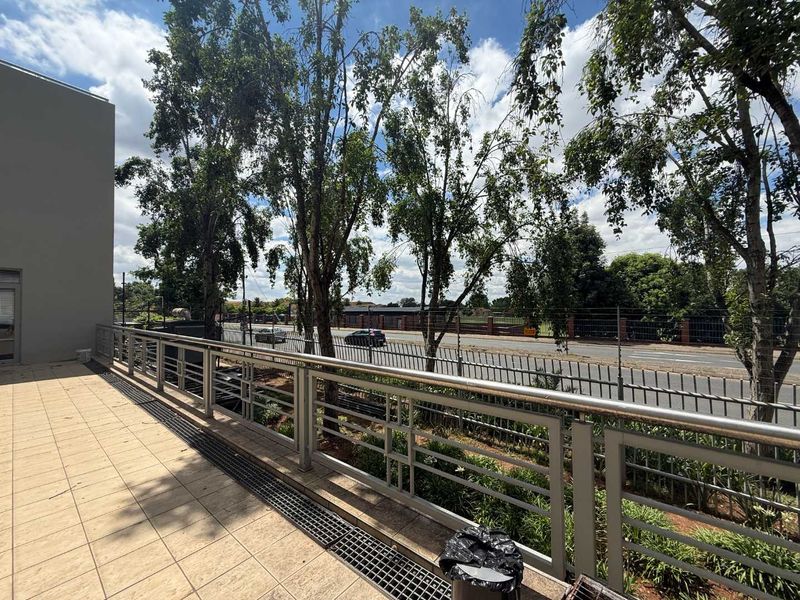 An elevated outdoor balcony area featuring tiled flooring and a secure metal balustrade overlooking the street and surrounding greenery.