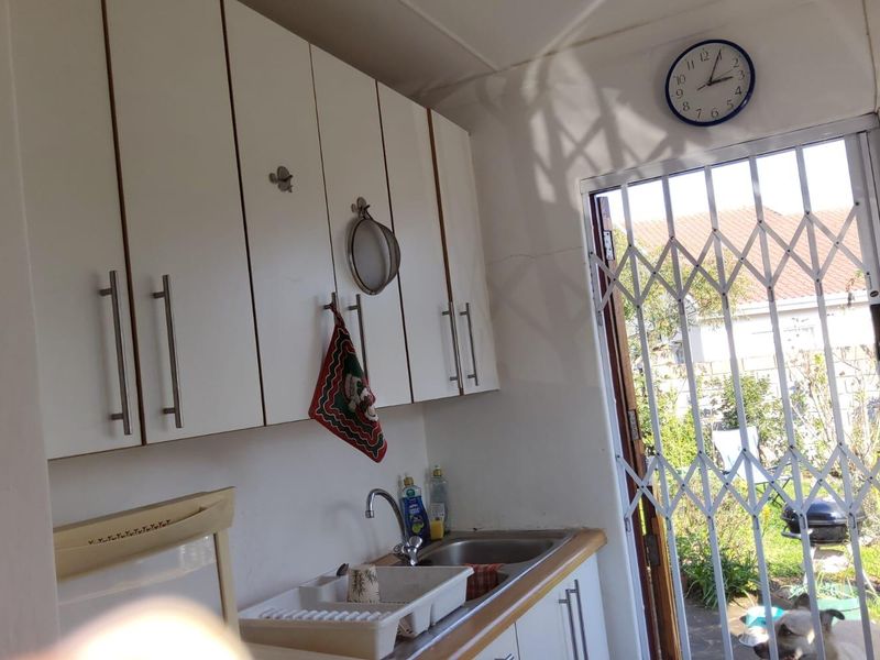 A functional scullery area featuring built-in white cabinetry, a stainless steel sink, and direct access to the rear garden through a security gate.