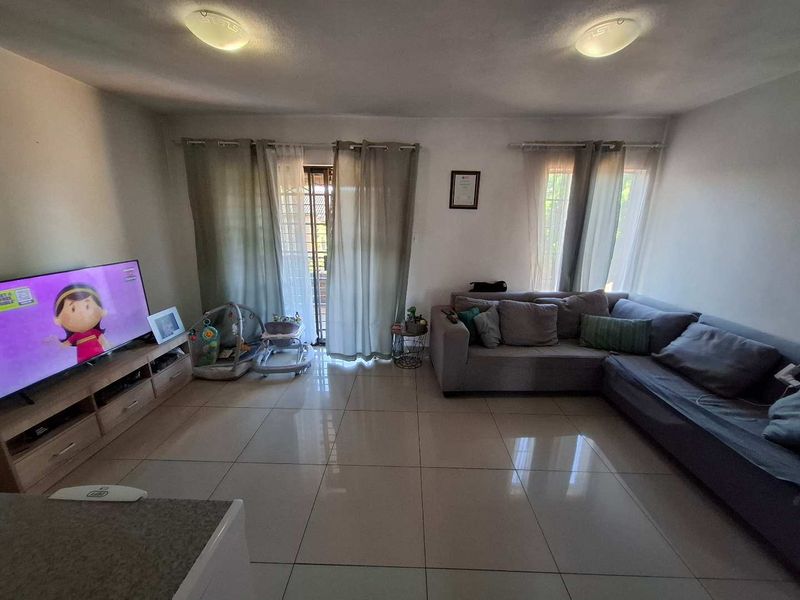 A spacious living room featuring large format floor tiles, neutral walls, and a sliding glass door providing access to the exterior.