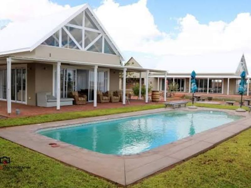 A spacious outdoor pool area featuring a well-maintained swimming pool, paved surround, and a covered patio attached to a modern farmhouse-style dwelling.