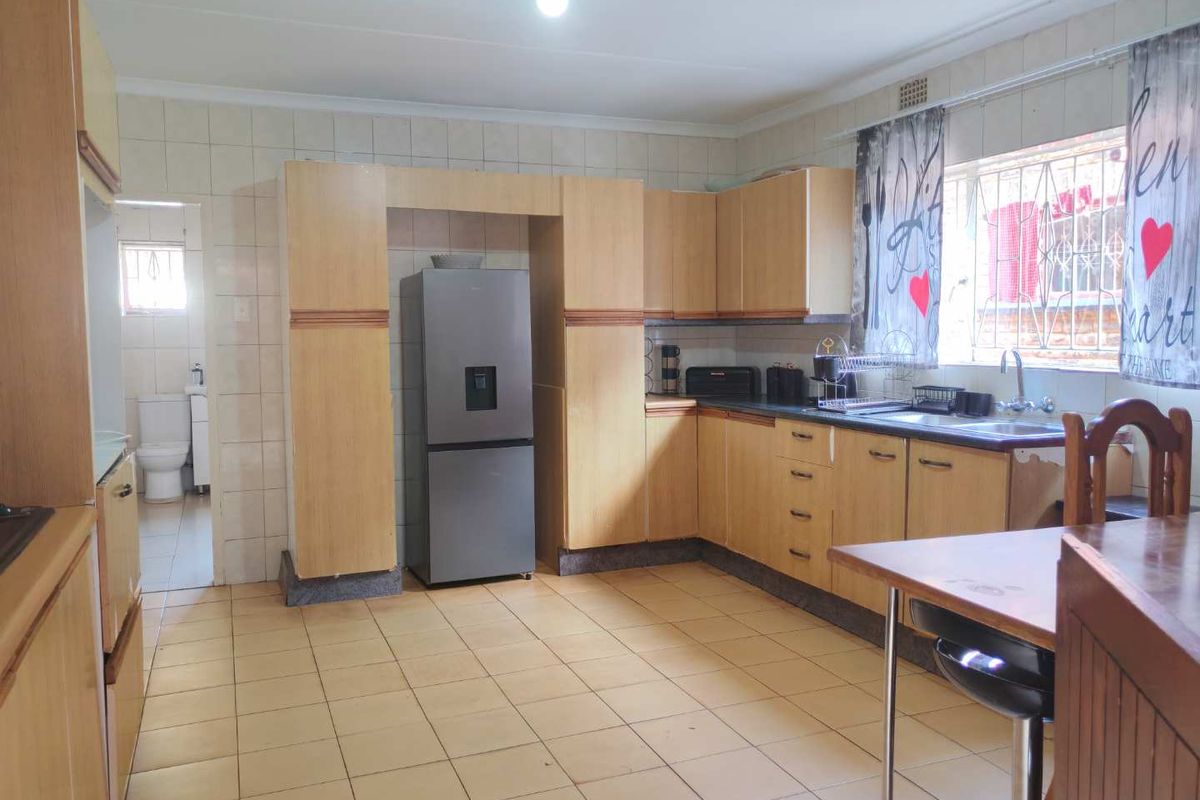 A functional kitchen featuring light wood-tone cabinetry, tiled flooring, and a tiled backsplash, with an adjacent utility area visible.