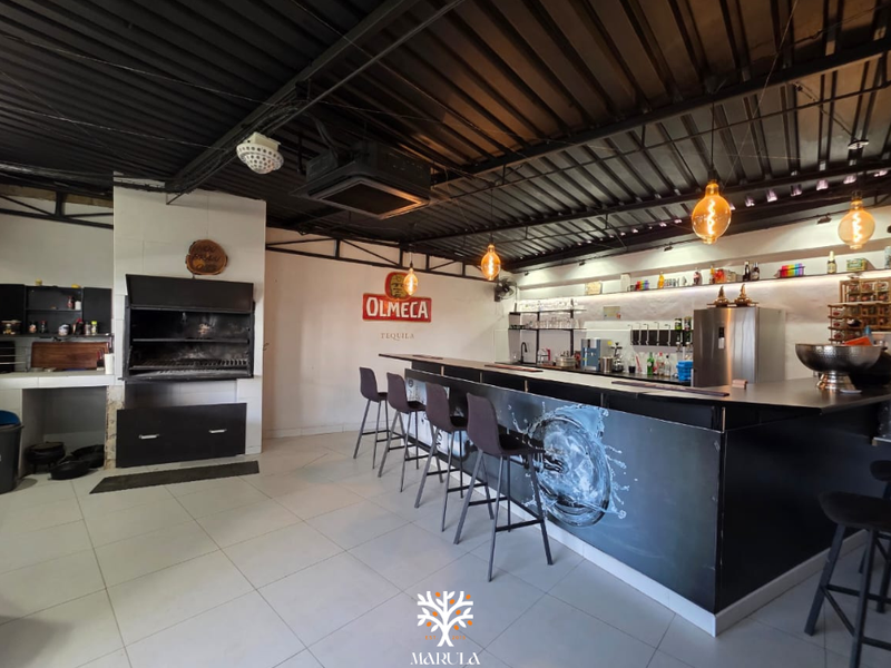 A well-appointed entertainment bar area featuring a built-in braai, sleek bar counter, and modern industrial-style exposed ceiling with pendant lighting.
