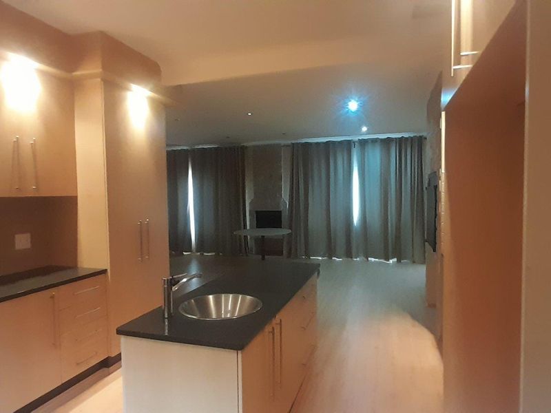Spacious open-plan living area featuring a modern kitchen with a central island, sleek cabinetry, and a cozy fireplace in the adjacent lounge space.