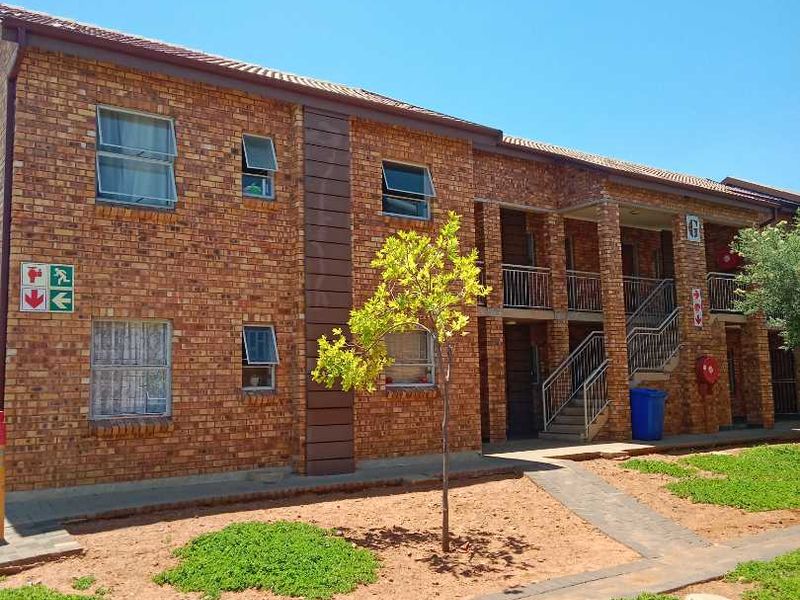 Exterior view of a multi-story apartment block featuring face brick construction, metal staircases, and paved communal garden walkways.