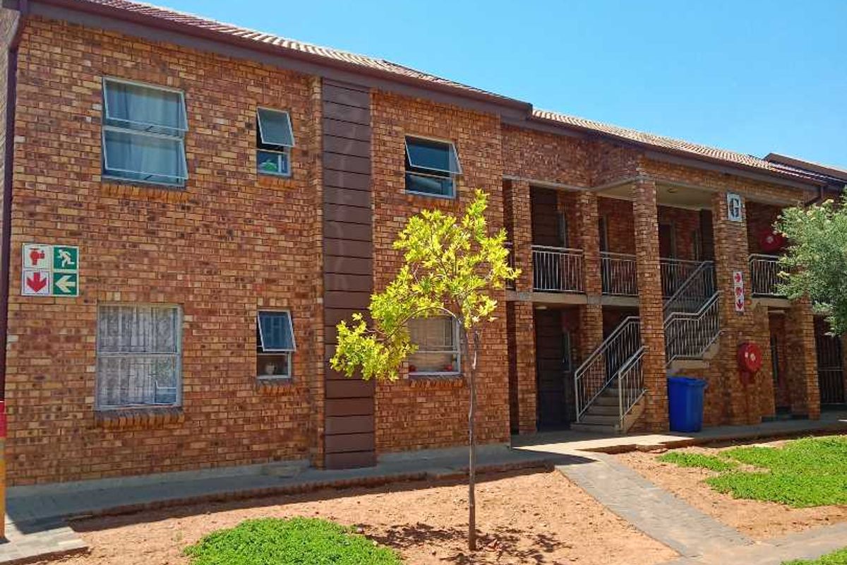 Exterior view of a multi-story apartment block featuring face brick construction, metal staircases, and paved communal garden walkways.