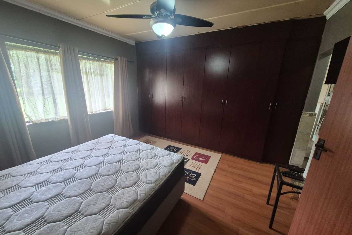 A bedroom featuring built-in dark wood cabinetry, laminate flooring, and a ceiling fan, offering ample storage space.