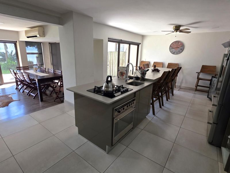 Spacious open-plan kitchen and dining area featuring a central island with gas hob, tiled flooring, and direct access to the outdoor patio.