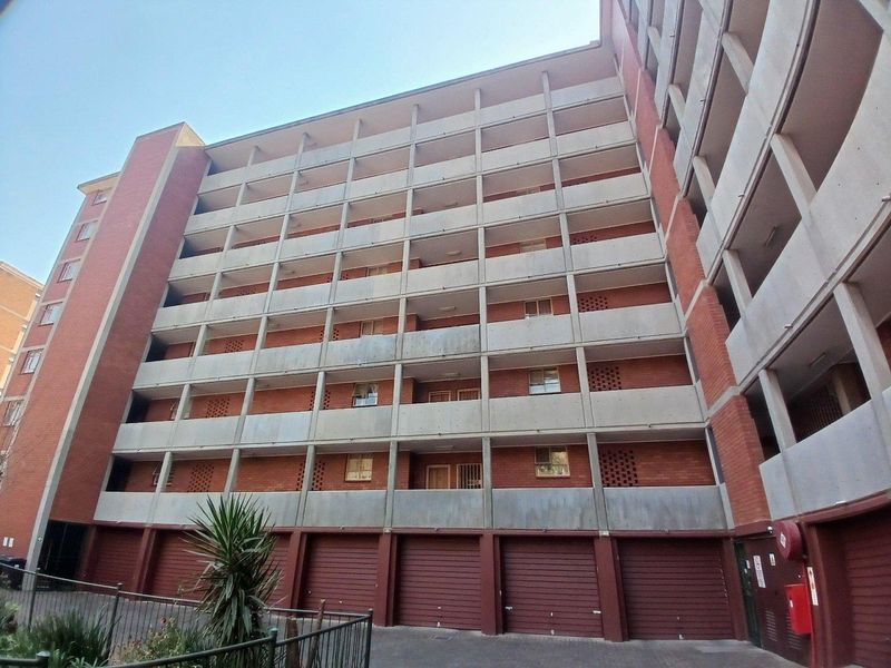 Exterior view of a multi-story apartment building featuring brick facade, concrete balconies, and ground-level garage access.