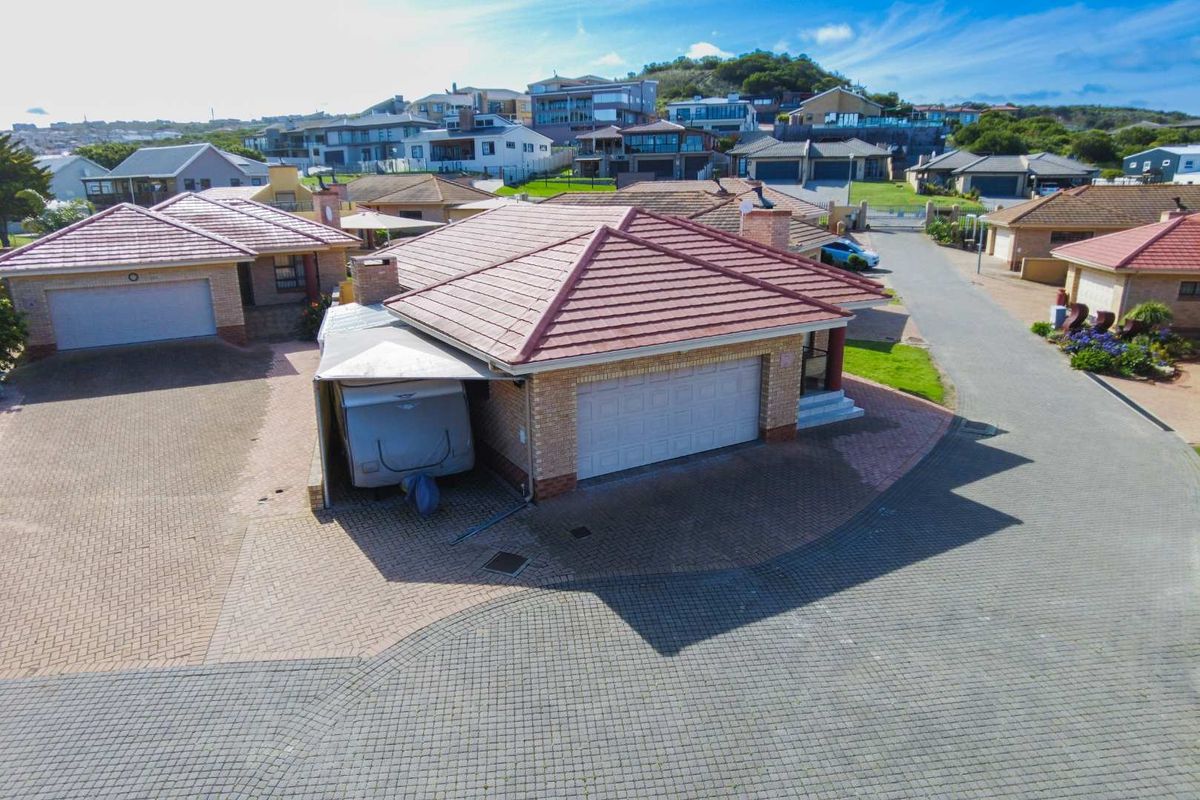 Aerial view of a residential townhouse property featuring a tiled roof, brick exterior, double garage, and paved driveway within a suburban estate.