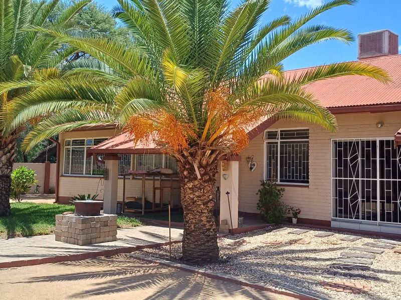 Rear exterior view of the house featuring a corrugated metal roof, brick walls, security bars on windows, and a landscaped garden area.