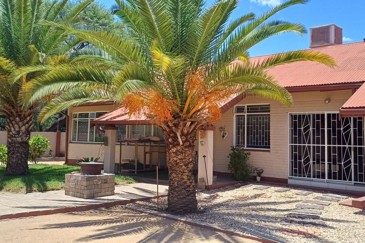 Rear exterior view of the house featuring a corrugated metal roof, brick walls, security bars on windows, and a landscaped garden area.