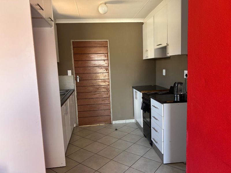 A functional kitchen featuring white cabinetry, dark countertops, a freestanding stove, and tiled flooring, providing a practical workspace with direct access to an exterior door.