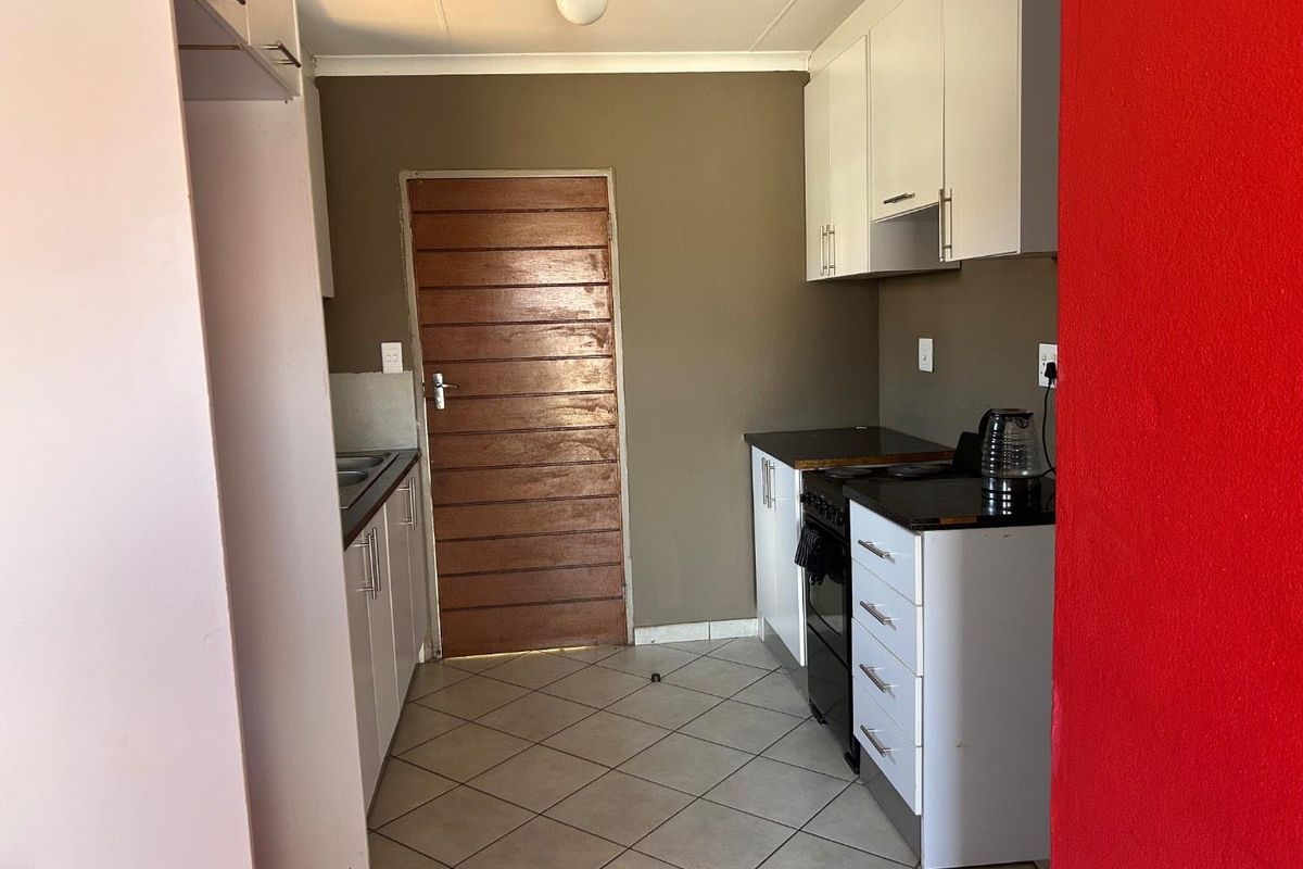 A functional kitchen featuring white cabinetry, dark countertops, a freestanding stove, and tiled flooring, providing a practical workspace with direct access to an exterior door.