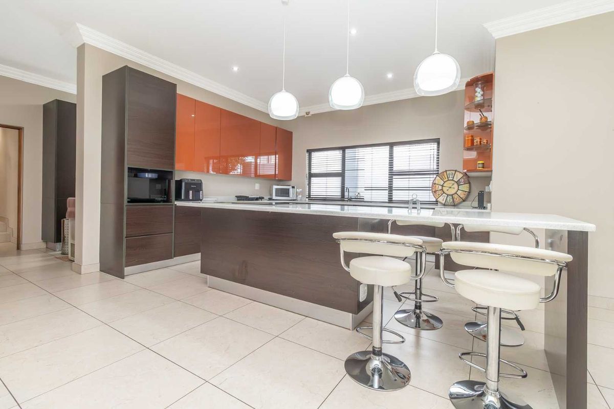 Modern kitchen featuring high-gloss orange and dark wood cabinetry, a central island with breakfast bar seating, and tiled flooring.