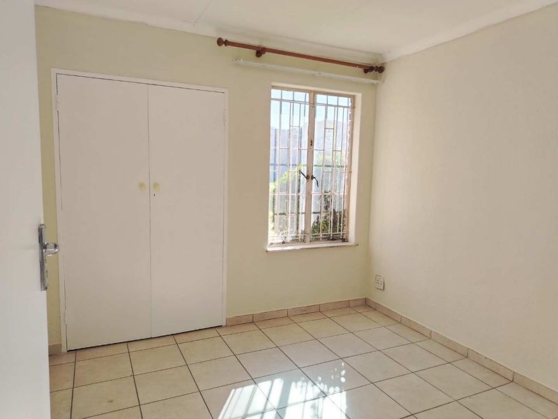A vacant bedroom featuring tiled flooring, a built-in wardrobe, and a window fitted with security bars.