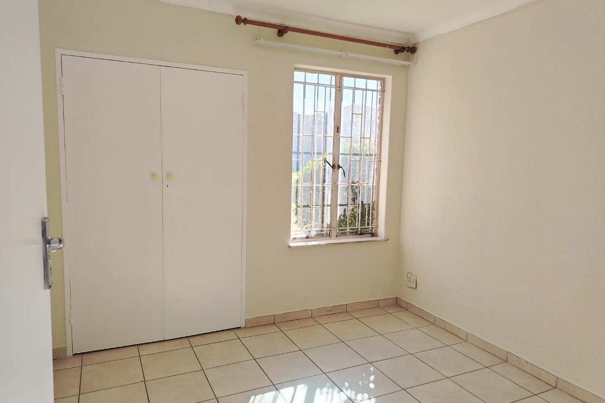 A vacant bedroom featuring tiled flooring, a built-in wardrobe, and a window fitted with security bars.