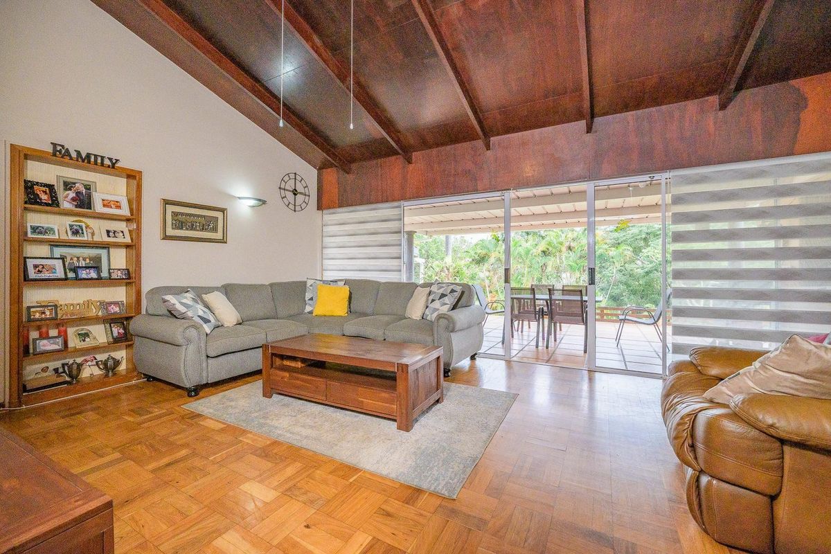 Spacious living room featuring high exposed timber beam ceilings, classic parquet flooring, and large sliding glass doors providing seamless access to the outdoor patio area.