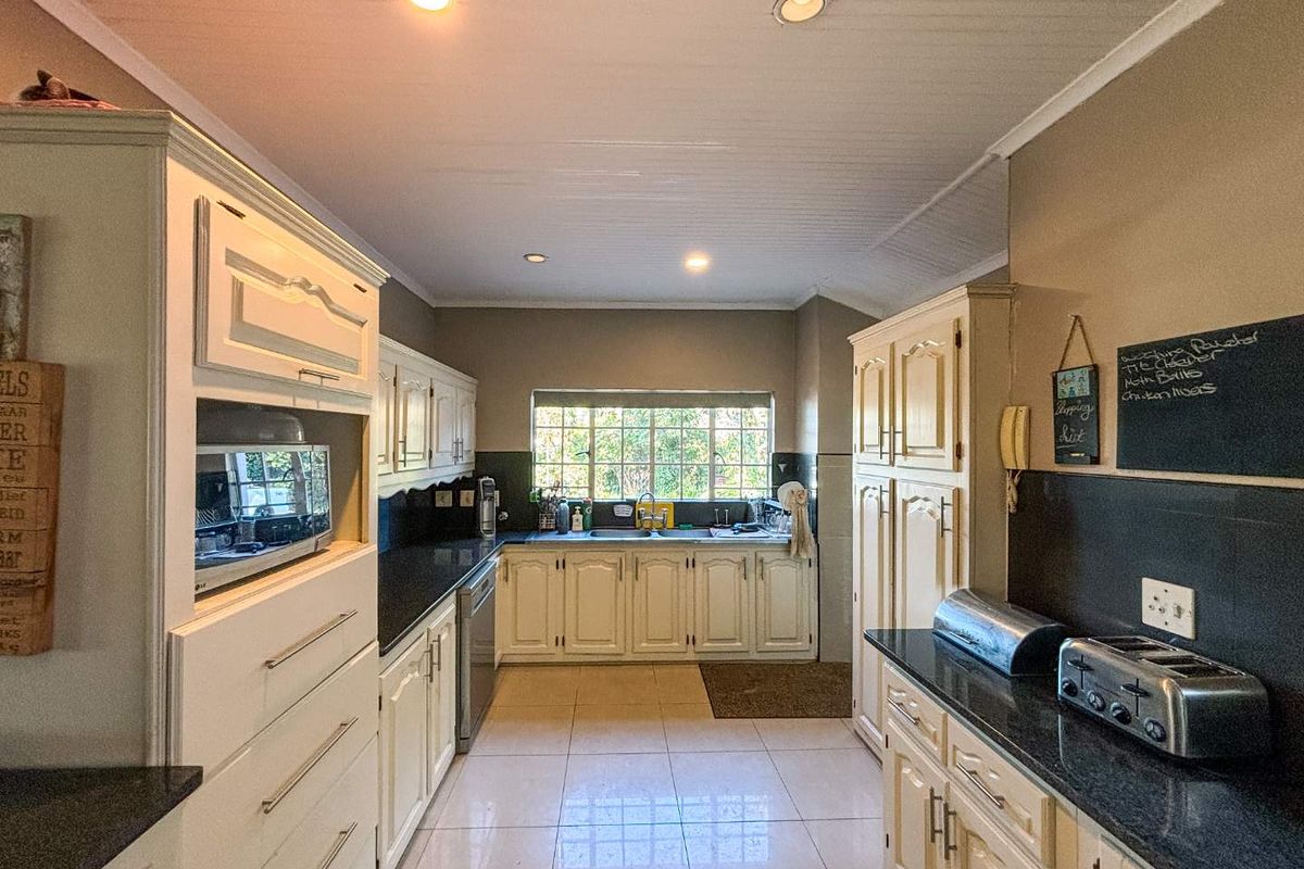 A functional kitchen featuring cream-colored cabinetry, dark granite countertops, a double sink, and recessed ceiling lighting.