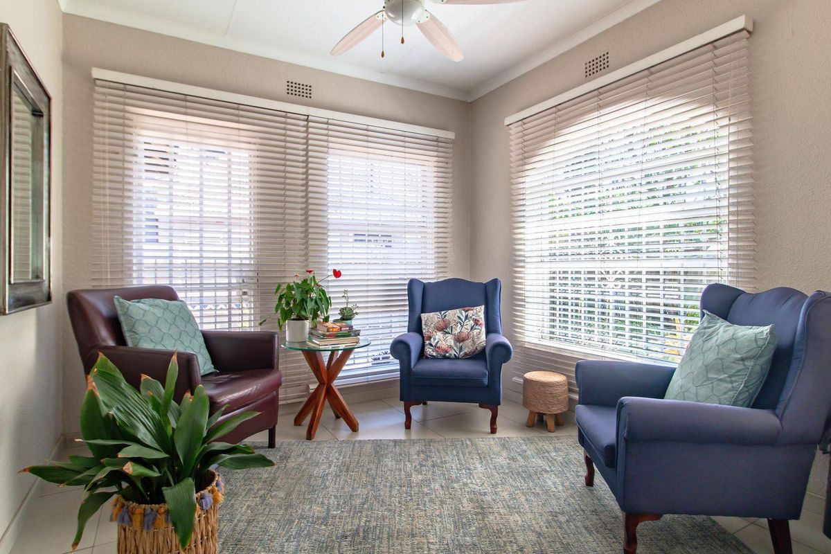 A bright living room featuring large windows with fitted blinds, tiled flooring, and a ceiling fan.