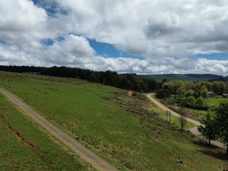 Aerial view of a large, sloped vacant residential plot featuring established access roads, surrounding greenery, and scenic landscape views.