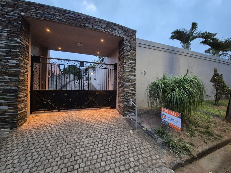 A secure front entrance featuring a stone-clad portal, wrought iron gate, and a cobblestone driveway leading to the property.