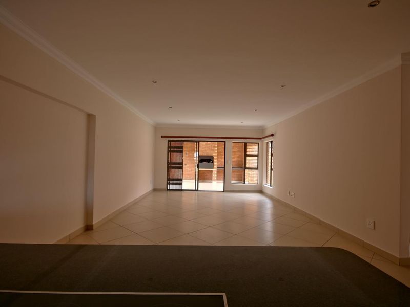 Spacious open-plan living area featuring neutral tiled flooring, recessed lighting, and sliding glass doors leading to an outdoor patio with a built-in braai.