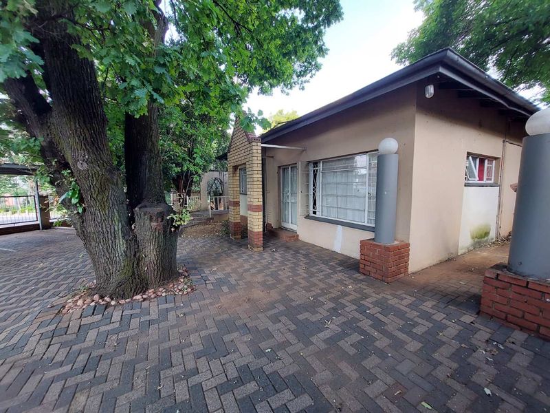 Front exterior view of the apartment featuring a paved driveway, brick pillar accents, and mature trees, showing signs of exterior wall maintenance required.