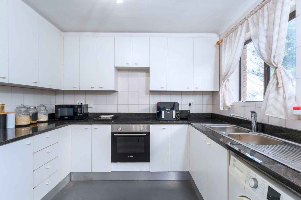 A functional kitchen featuring white cabinetry, dark granite countertops, a built-in oven, and a double stainless steel sink with integrated plumbing for appliances.