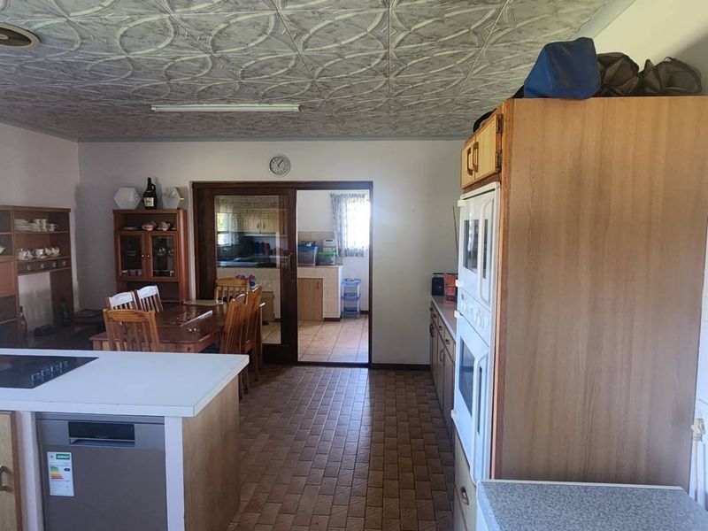 Open plan kitchen and dining area featuring dated cabinetry, built-in oven, hob, and tiled flooring with access to an adjacent scullery area.