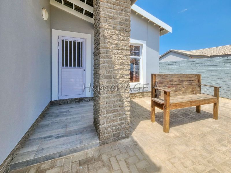 A clean, paved patio area featuring a brick support pillar and a secure entrance door with a security gate.