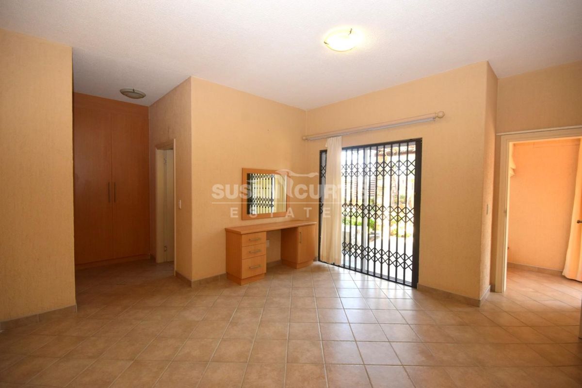 Spacious bedroom featuring tiled flooring, built-in cupboards, and a sliding door with a security gate providing access to the exterior.