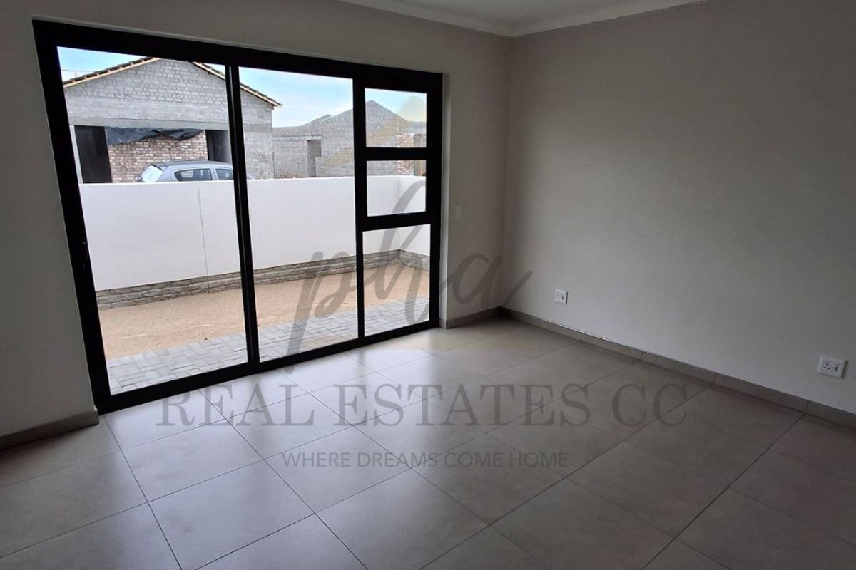 A bright, empty living room featuring large black-framed sliding glass doors that open onto a paved outdoor area.