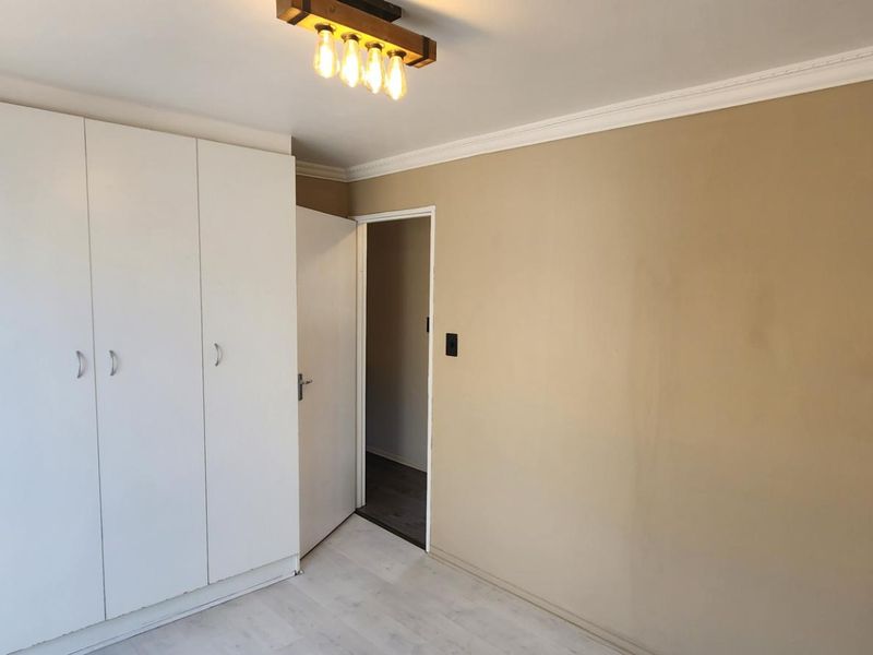 A clean, empty bedroom featuring built-in white cupboards, laminate flooring, and decorative ceiling coving.